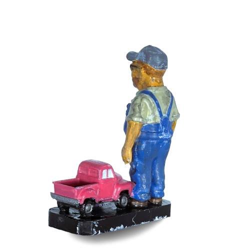 Figura de jubilado con mono azul, vista trasera tres cuartos, junto a camioneta rosa con base 'Feliz Jubilación'

