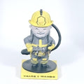 Figura 3D de bombero con manguera vista frontal, casco amarillo, barba gris y base con texto Valor y Mando