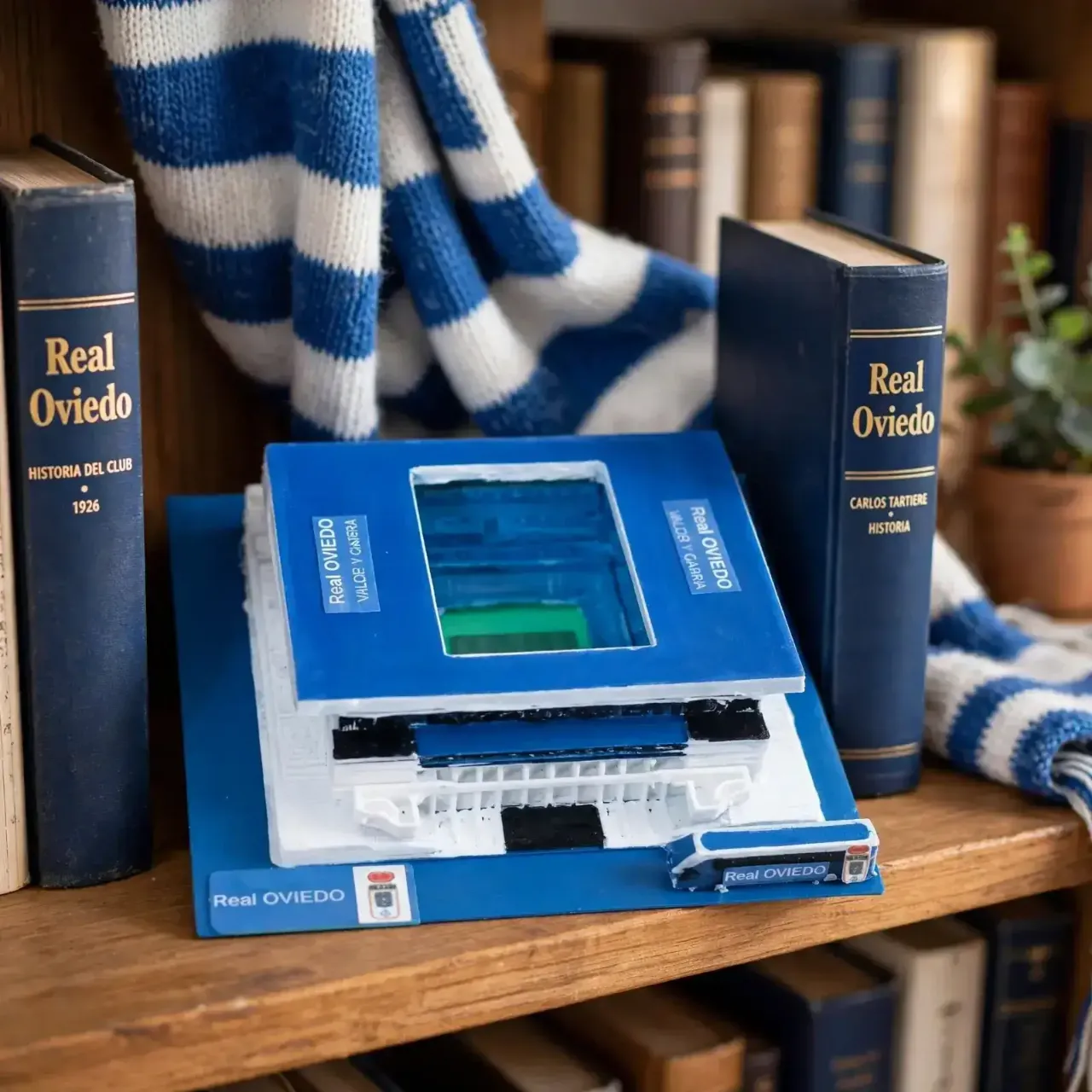 Maqueta del Carlos Tartiere del Real Oviedo en estantería entre libros de historia del club y bufanda azul y blanca