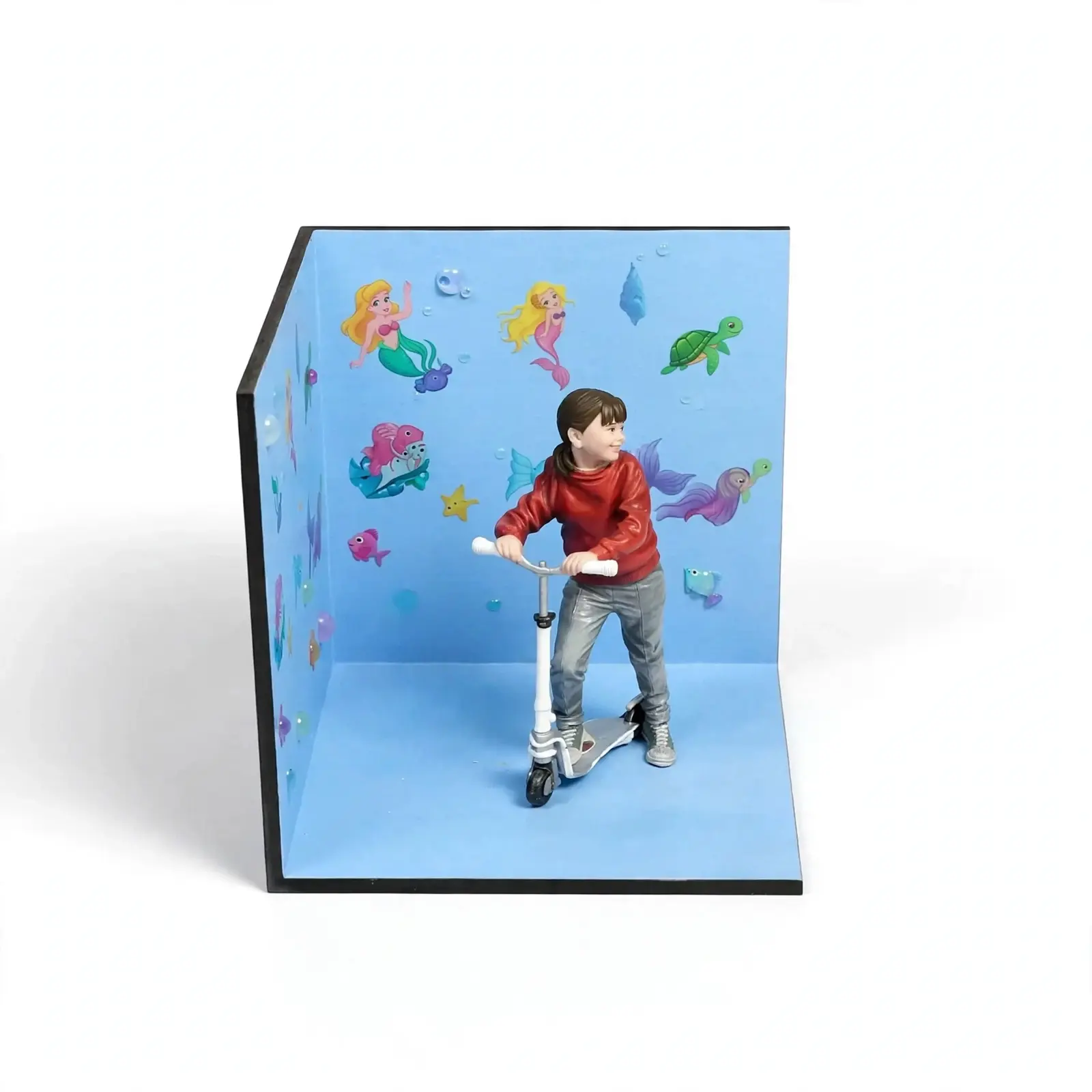 Detalle lateral de figura de niña sonriendo en patinete con sudadera roja y pantalón gris, diorama personalizado TRES D